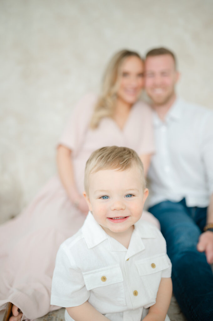 Boy smiling at camera with parents sitting behind him. Taken by Gabrielle Crowley Photography. 